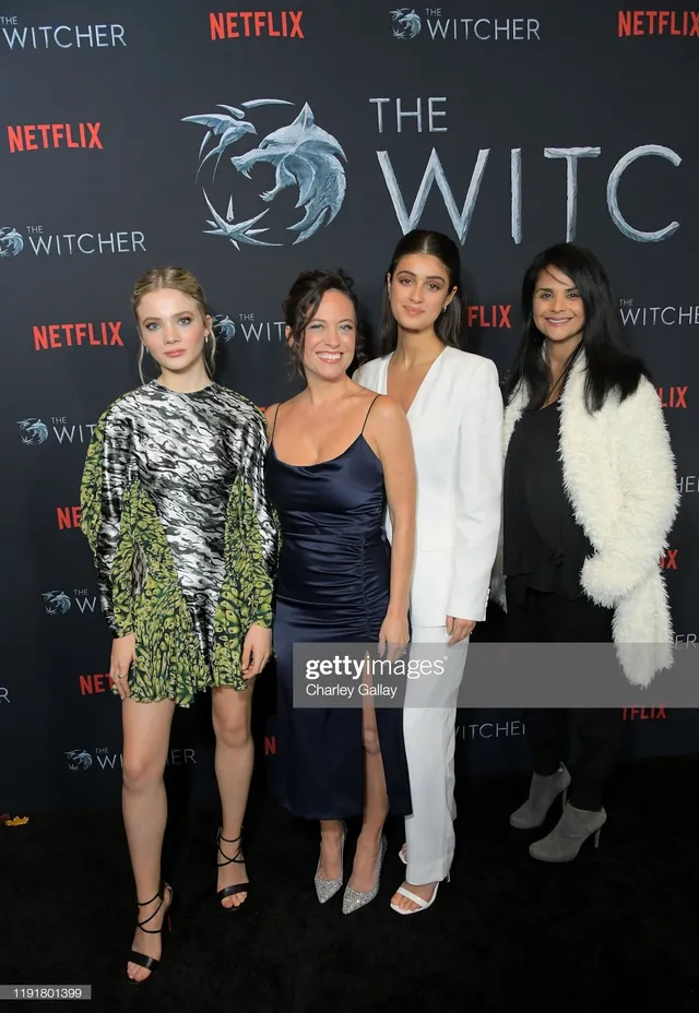 Anya Chalotra posing with three women at a premiere in a white suit and heels.
