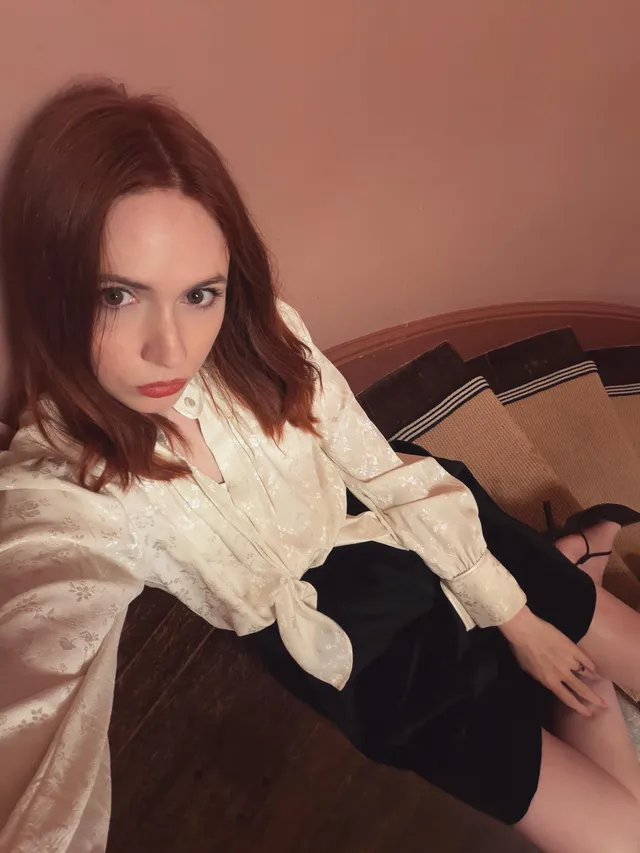 Karen Gillan sitting in a pale blouse and dark skirt for a casual photo.