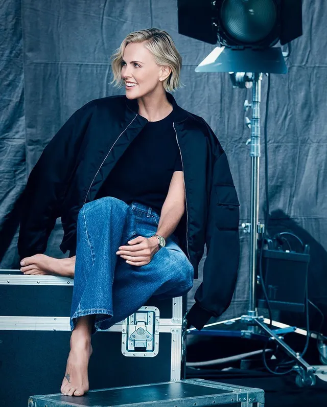 Charlize Theron seated backstage in jeans and a dark jacket.