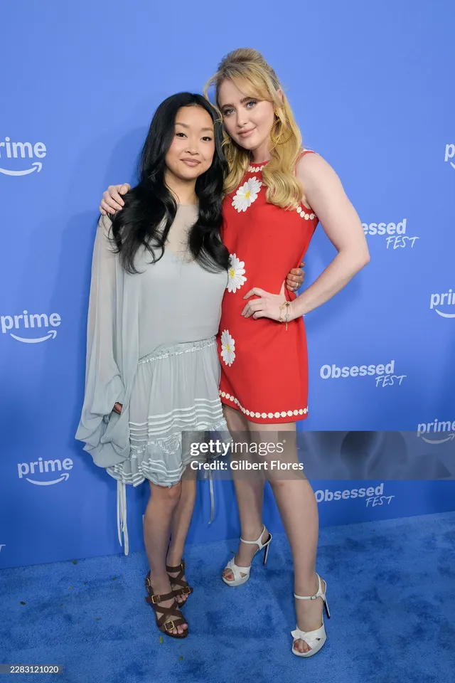 Kathryn Newton posing beside another woman in a red dress and pale heels.