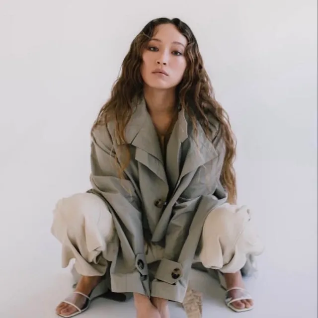 Havana Rose Liu crouching in pale trousers and white heels.