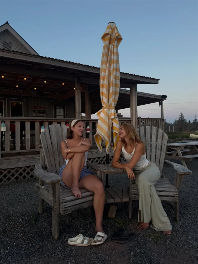 Sophie Nélisse sitting barefoot beside another woman on a veranda.