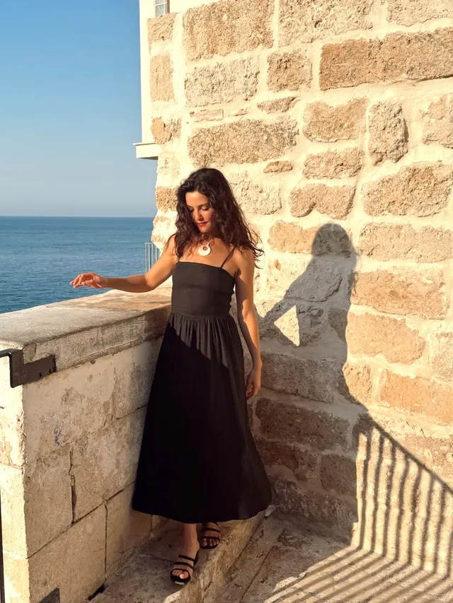 Danielle Campbell standing beside a stone balcony in a black dress.
