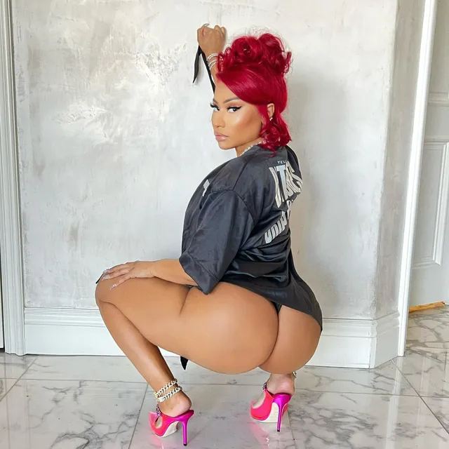 Nicki Minaj crouching indoors in pink heels.
