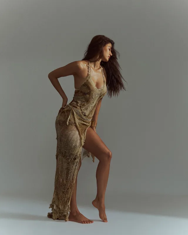 Disha Patani posing barefoot in a gold outfit with one heel raised.