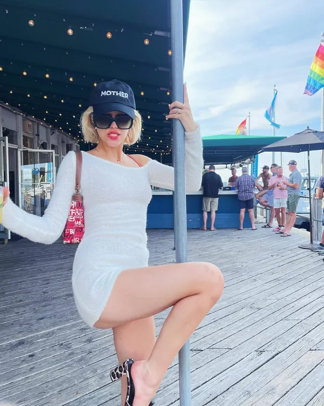 Grace VanderWaal standing on a boardwalk in a white dress and black heels.