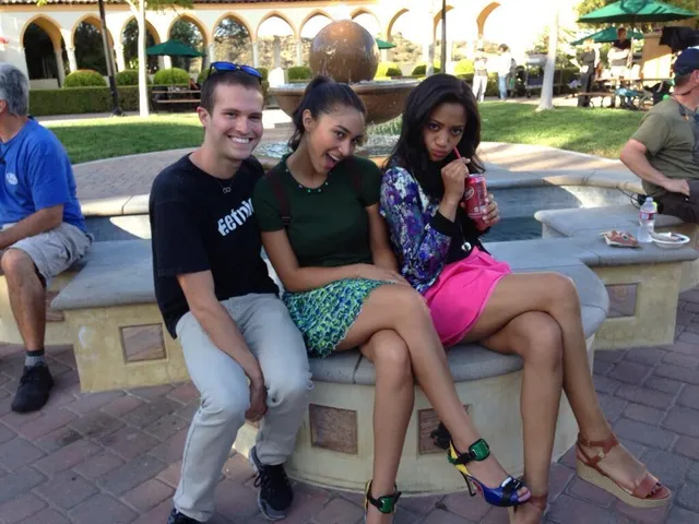 Samantha Logan sitting with friends outdoors in a patterned top, pink skirt and brown heels.