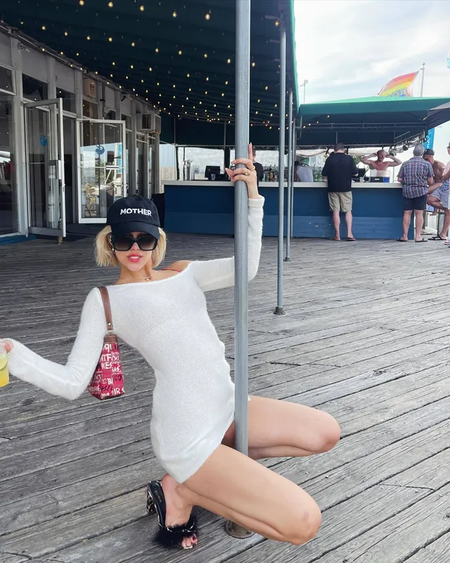 Grace VanderWaal posing beside a pole on a wooden boardwalk wearing black heels.