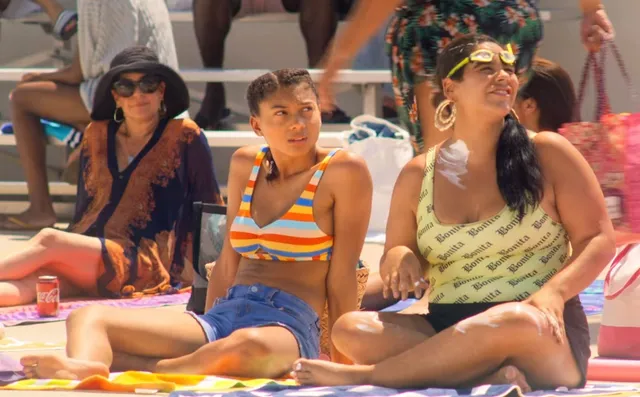 Sierra Capri sitting barefoot beside a pool with a friend in a scene.