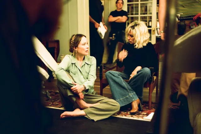 Olivia Wilde sitting cross-legged on a sofa with bare feet visible in a film scene.