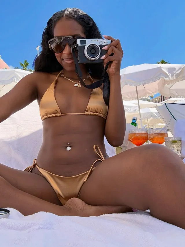 Carlacia Grant sitting on a beach lounger in a gold bikini with bare legs.