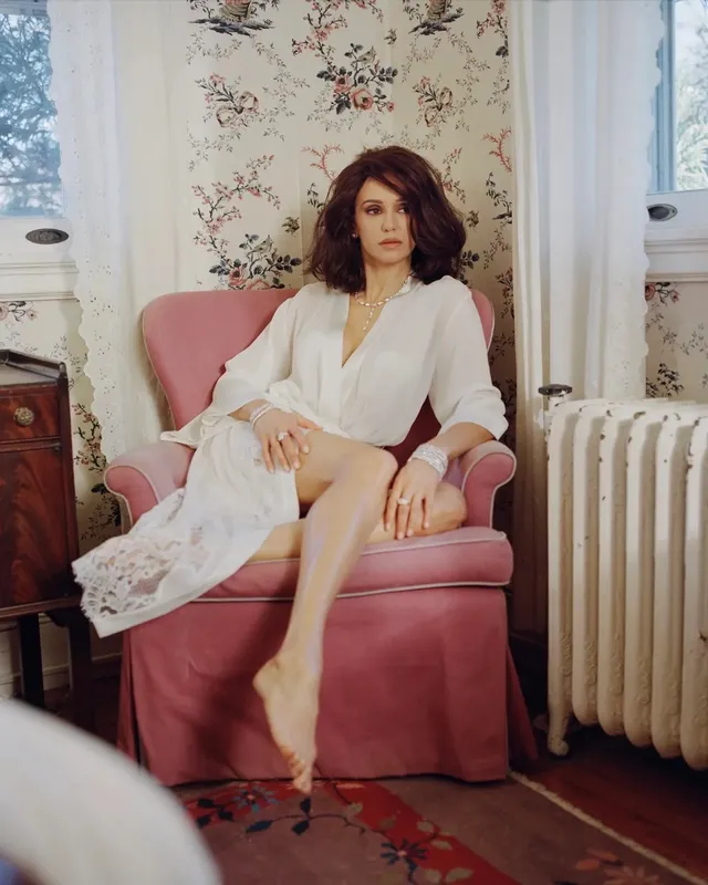 Nina Dobrev sitting barefoot in a pink armchair.