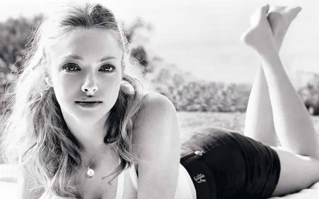 Amanda Seyfried lying outdoors with bare feet raised in a monochrome portrait.