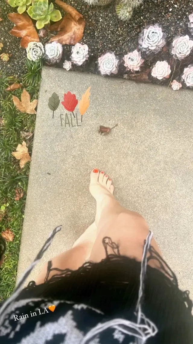 Avril Lavigne standing barefoot beside an outdoor display.