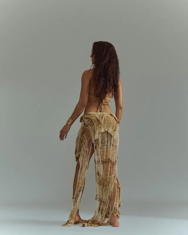 Disha Patani standing barefoot in a fringed gold outfit during a studio shoot.