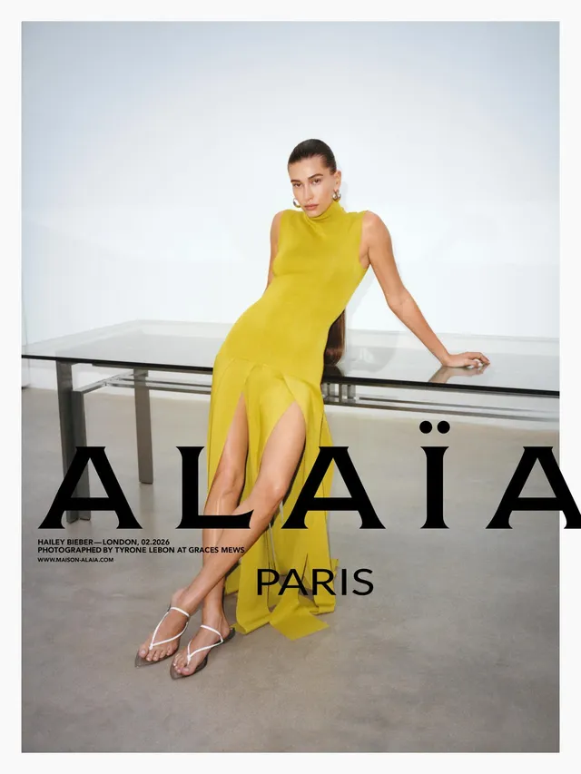 Hailey Bieber wearing a yellow dress and clear sandals in a studio.