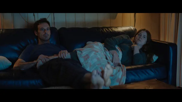 Amy Adams reclining with a companion on a sofa during a screen scene.
