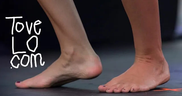 Tove Lo standing barefoot in a close-up stage photograph.