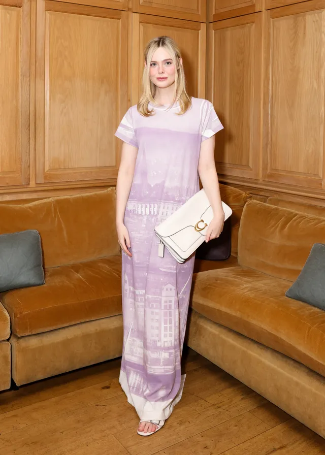 Elle Fanning wearing a pale lavender outfit and sandals indoors.
