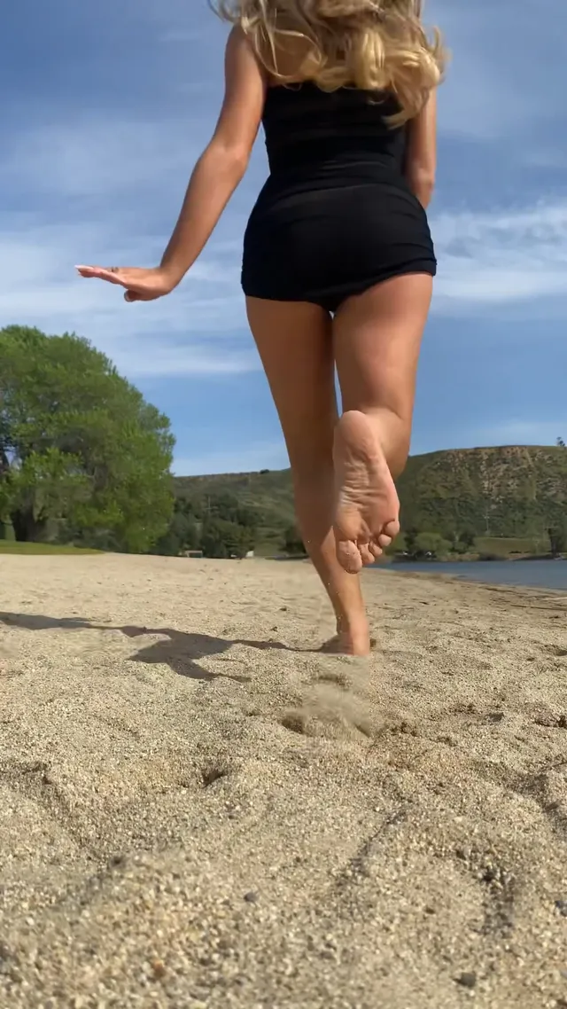 Sabrina Carpenter: standing barefoot in sand in a black outfit.