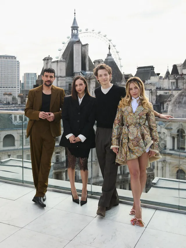 Florence Pugh posing with a group on a rooftop in a patterned outfit and heels.
