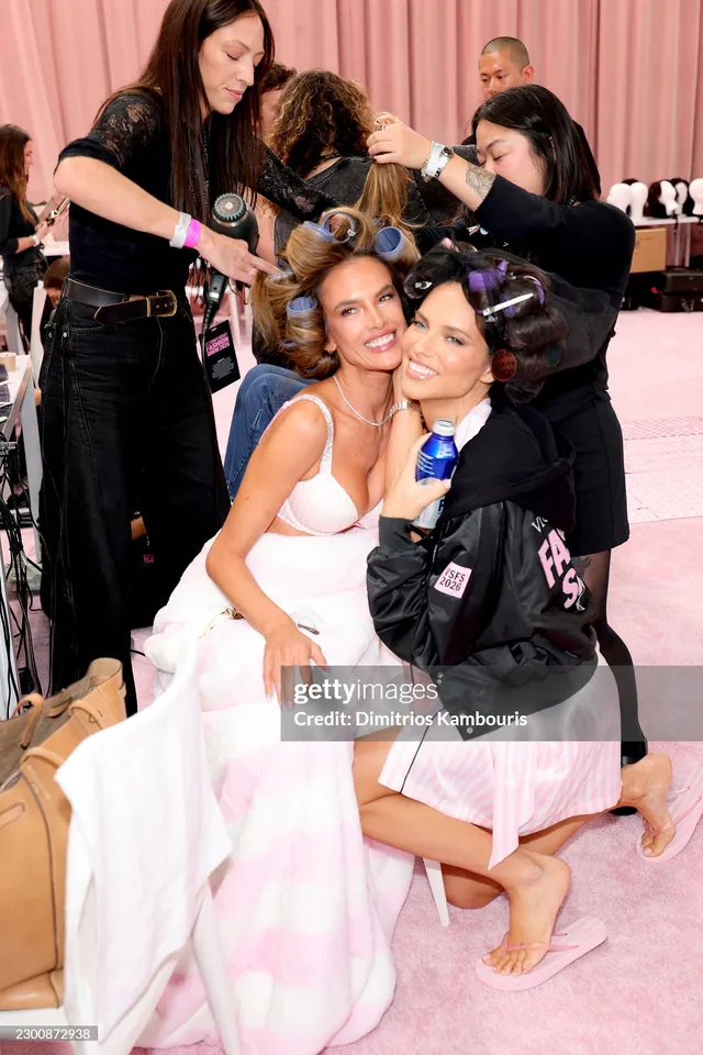 Adriana Lima seated backstage in a pink robe with a bare foot raised.