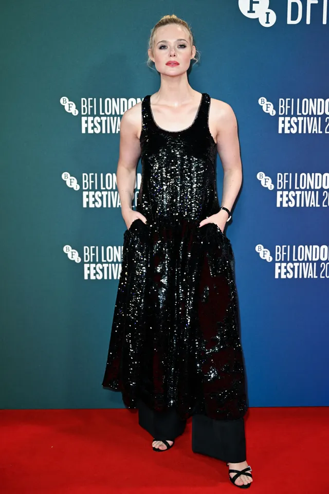 Elle Fanning posing on a red carpet in a black outfit and heeled sandals.