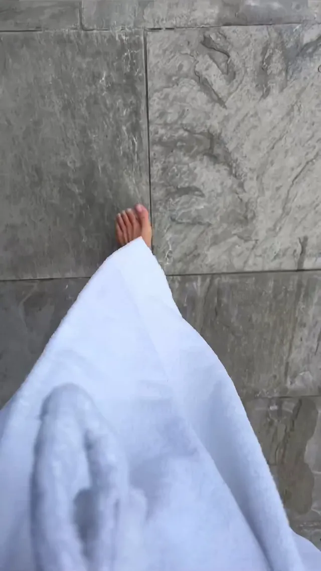 Kiana Madeira shown walking barefoot on a stone floor in a white robe.