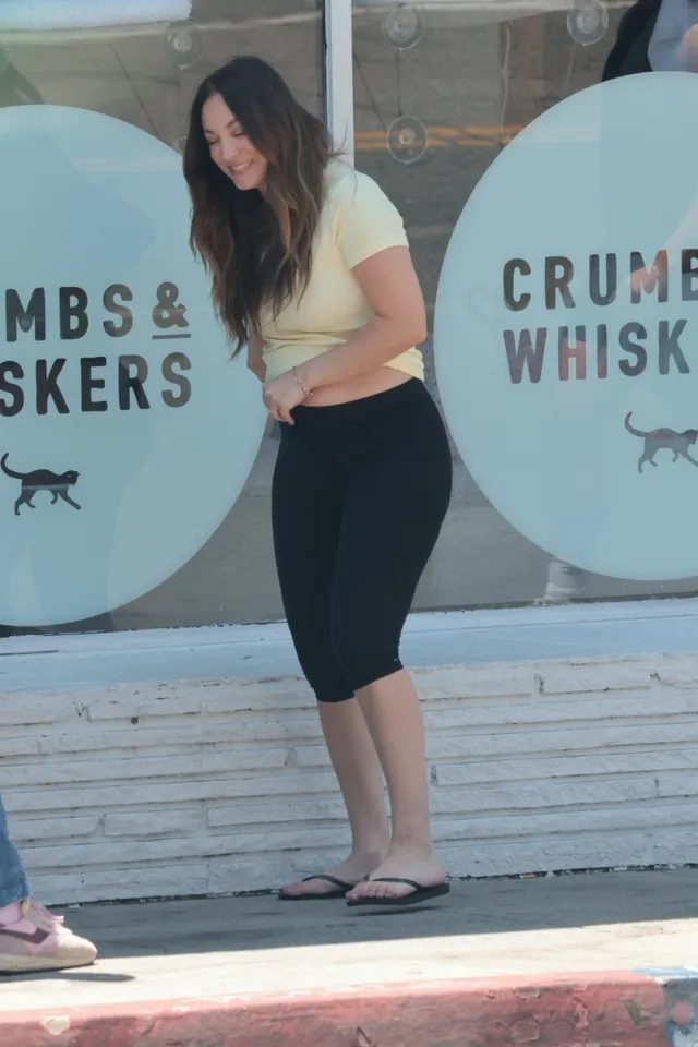 Kaley Cuoco walking outside a shop in black leggings and flip-flops.
