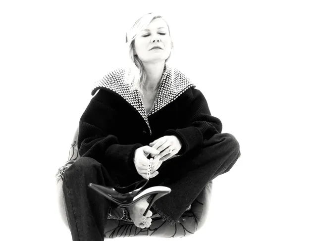 Kirsten Dunst sitting cross-legged in a black outfit for a monochrome portrait.