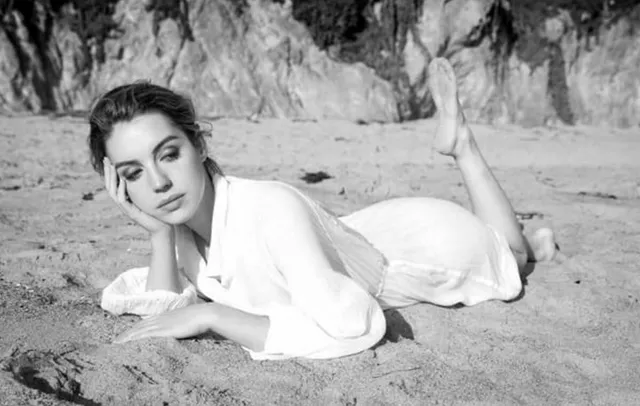 Adelaide Kane reclining on sand for a black-and-white portrait.