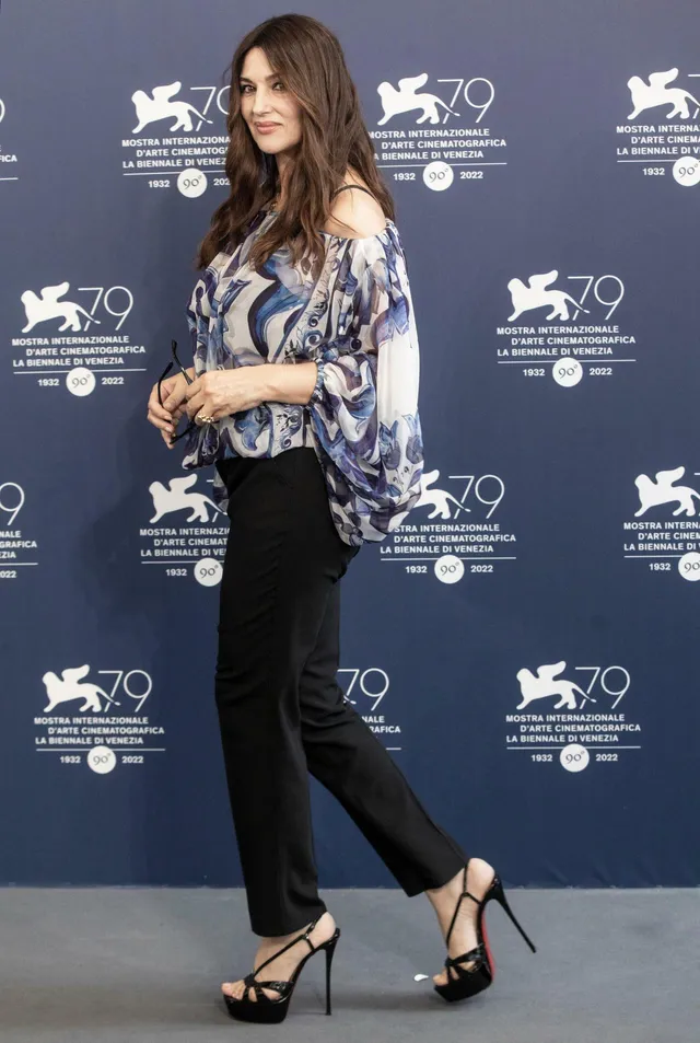 Monica Bellucci posing at a film festival in dark trousers and heels.