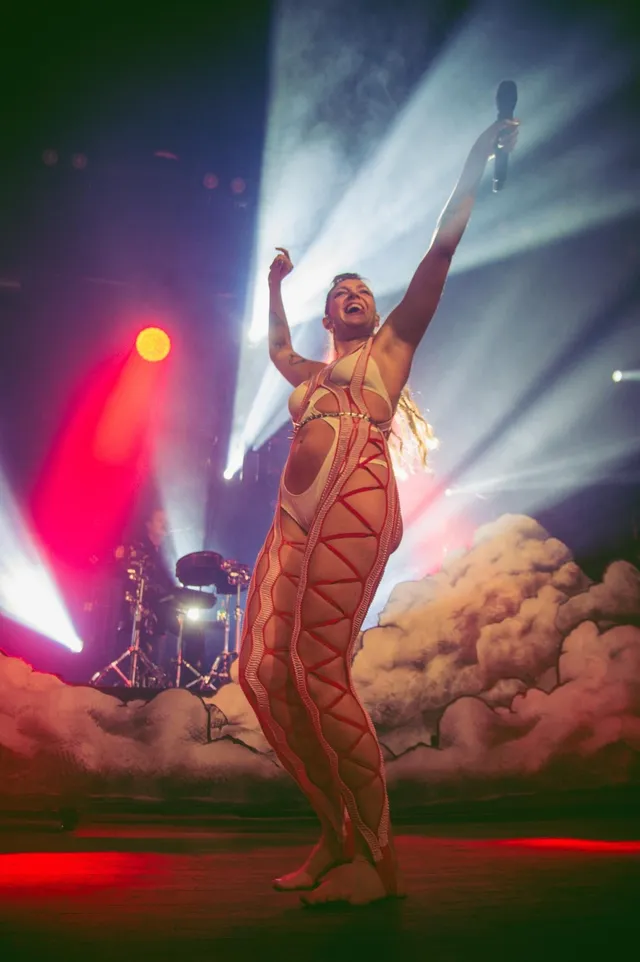 Tove Lo performing barefoot on stage with arms raised.