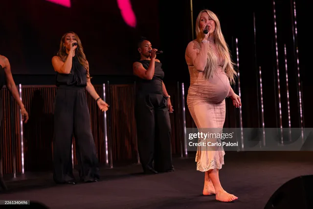 Ellie Goulding standing barefoot on stage in a pale dress.