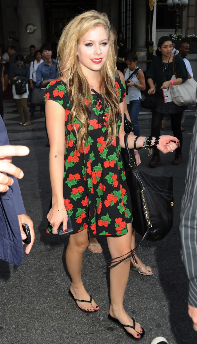 Avril Lavigne walking outdoors in a floral dress and flip-flops.