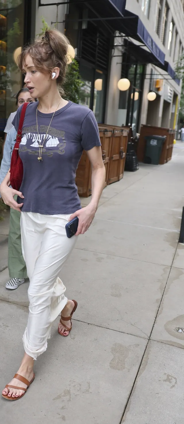 Jennifer Lawrence walking outside in a T-shirt and flat sandals.