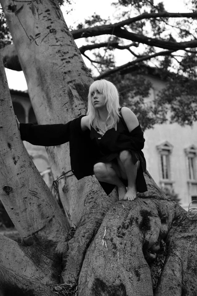 Billie Eilish a crouched monochrome portrait beside a tree.