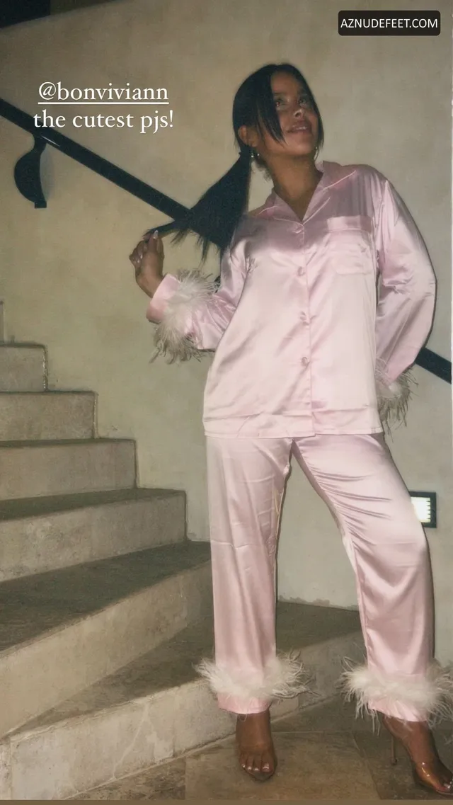 Cierra Ramirez in pink satin pajamas and platform sandals beside a staircase.