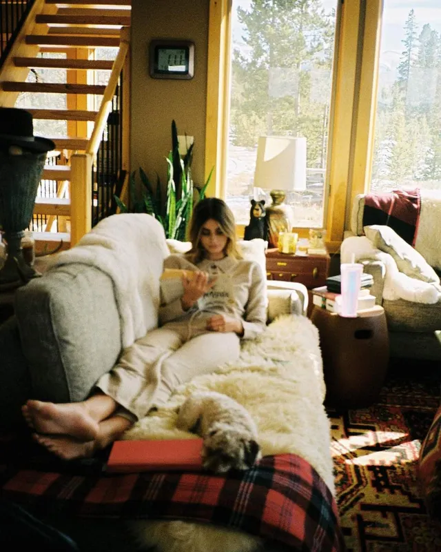 Taylor Hill reclining barefoot in an armchair beside a dog.