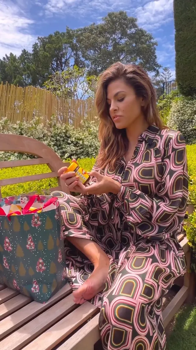 Eva Mendes sitting outside with a drink in a patterned dress.