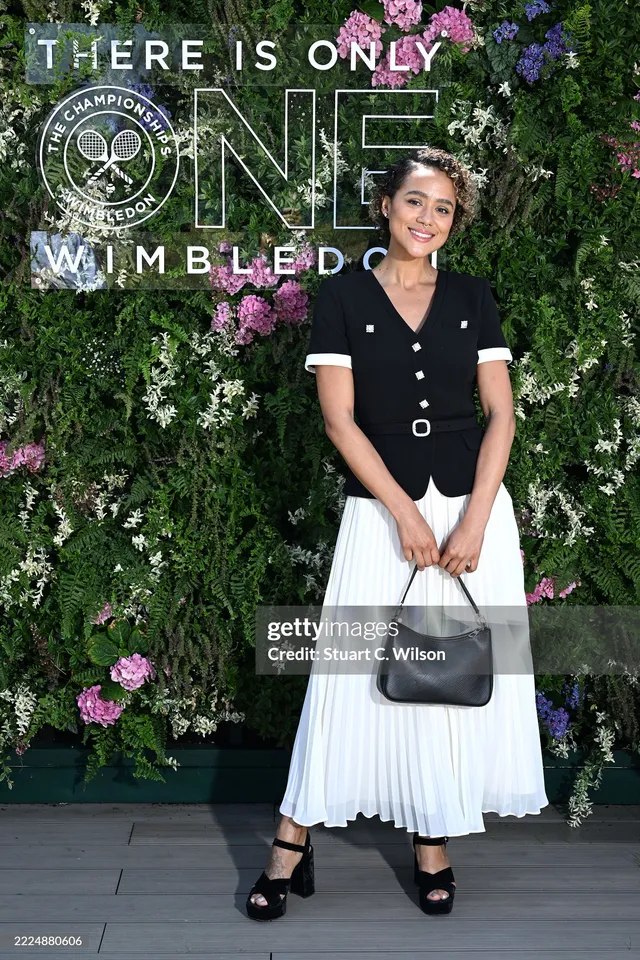 Nathalie Emmanuel posing at an outdoor event in a black top and white skirt.