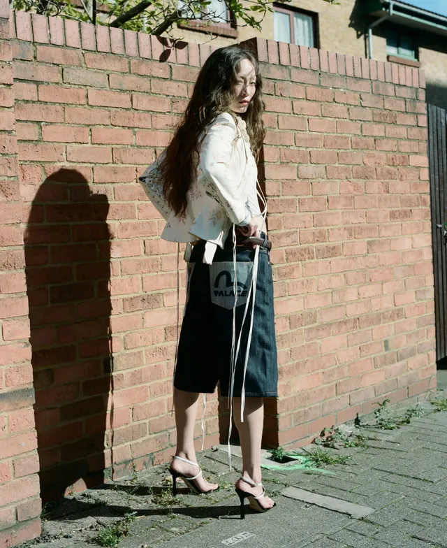 Havana Rose Liu posing by a brick wall in white heels.