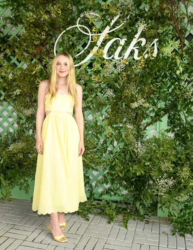 Dakota Fanning posing in a yellow dress and sandals at an event.