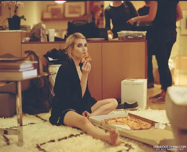 Emma Roberts sitting cross legged on the floor with pizza.