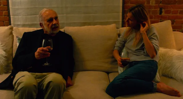 Sienna Miller talking with another character while seated.