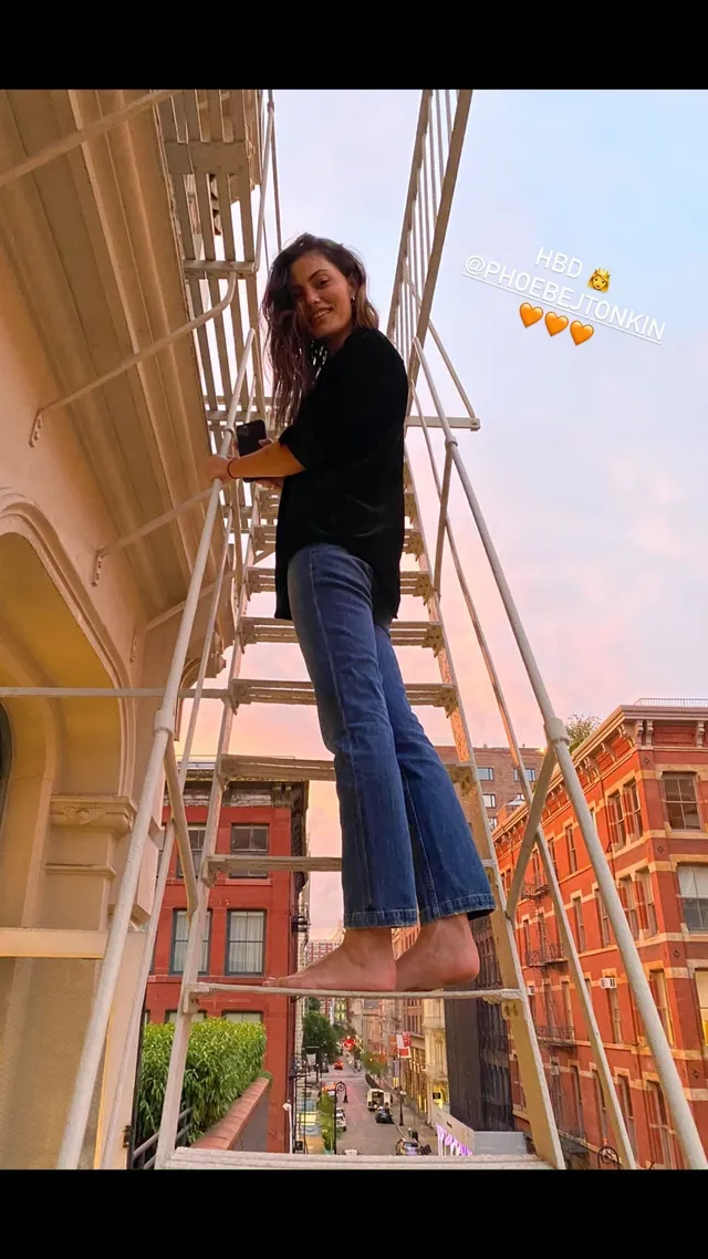 Phoebe Tonkin standing on a ladder outdoors.