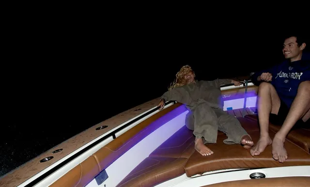 Iggy Azalea sitting barefoot on a boat beside another person at night.
