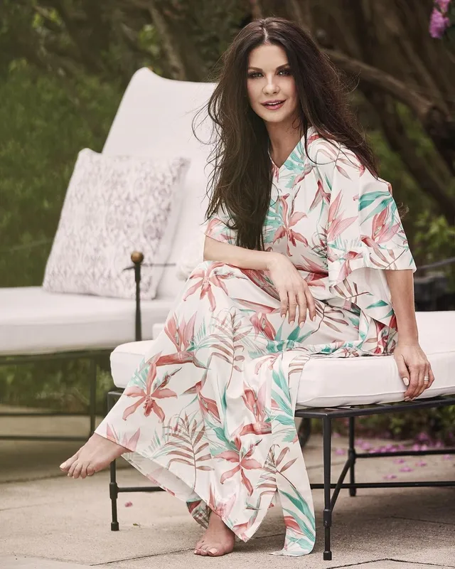 Catherine Zeta-Jones seated outdoors in a floral dress.