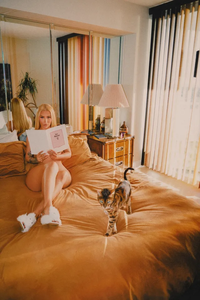 Iggy Azalea sitting on a bed beside a dog while reading.