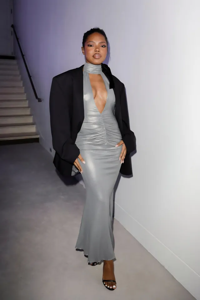 Ryan Destiny wearing a grey dress, black blazer and open-toe heels indoors.